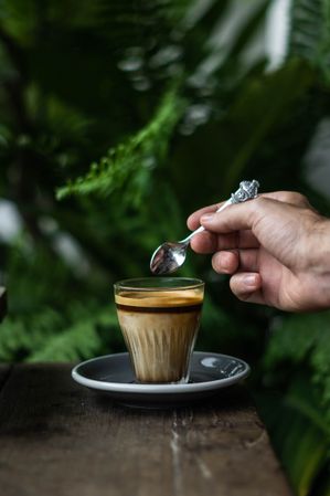 Cropped image of person holding a teaspoon over a cup of coffee