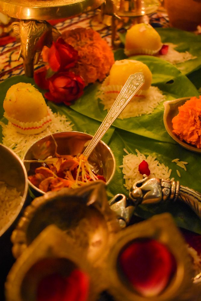 Saffron petals and ladoo surrounded by lit diyas on a table