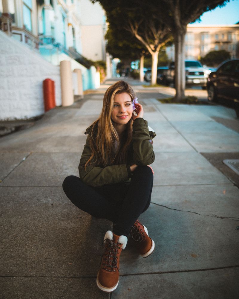 Woman in green jacket sitting on sidewalk