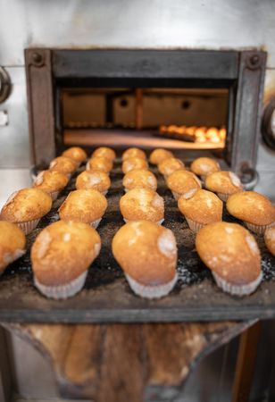 Some cupcakes tray freshly baked are being pulled from a stone oven with wooden shovel