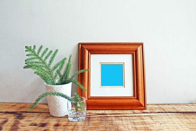 Square wooden picture frame on wooden desk with branches mockup