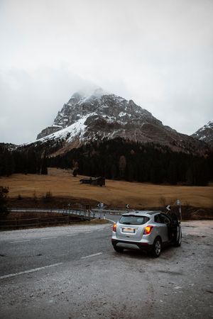 Lonely road with car on roadside among pine forest near big cliffs