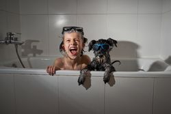 Cheerful boy with dog in bathtub