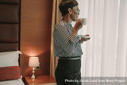 Businesswoman standing near in hotel room window with a cup of coffee 0yzlW5