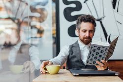 Man sits in window of trendy cafe with book