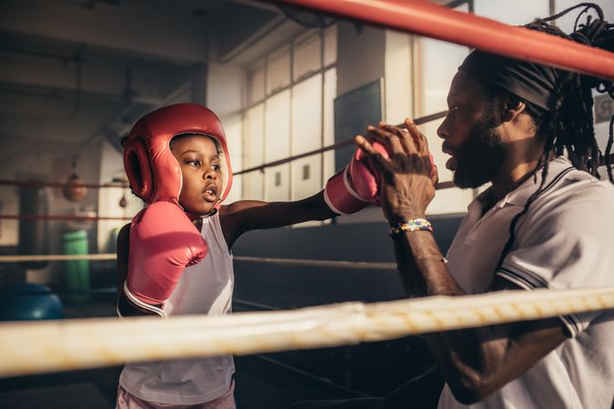 Student wearing boxing gloves and headgear hitting punches on hands of her trainer