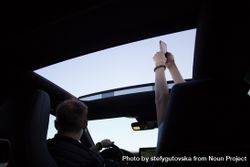 Two people having fun on a road trip taking photos out the sunroof 4Ayoq4