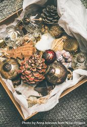 Wooden box of rustic holiday tree decorations, pine cones, balls and baubles laying on tissue paper bDEwQ0
