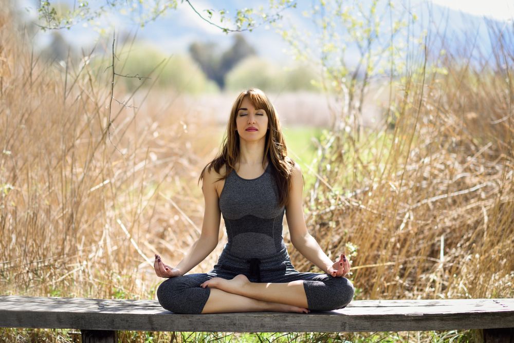 Young woman meditating on bench in nature with eyes closed
