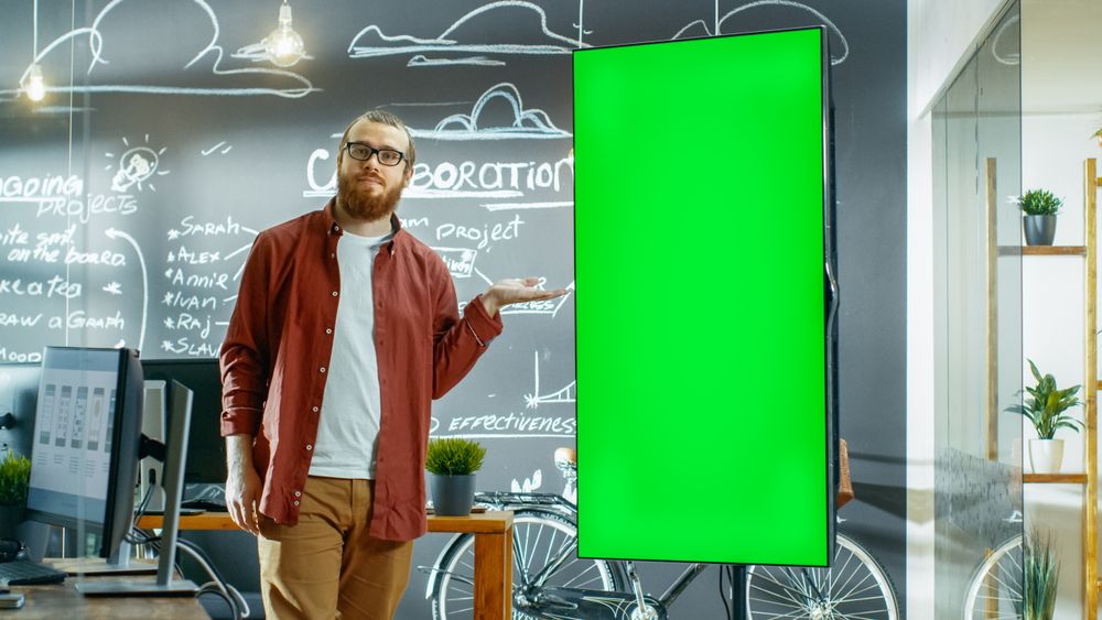 Male Developer Looks at Interactive Whiteboard with Mock-up Green Screen.