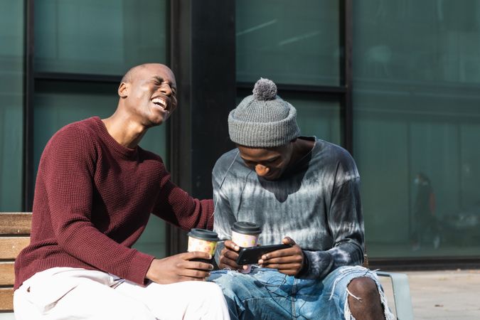 Excited Black friends sharing smartphone on street bench
