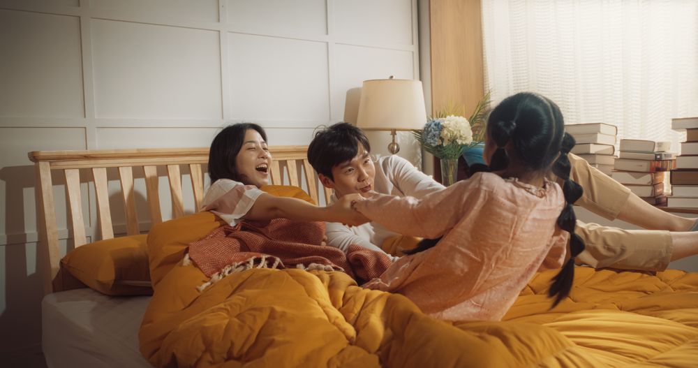 Happy Korean Family in the Morning: Active and Playful Child Running to her Parents' Bedroom to Wake Them Up.