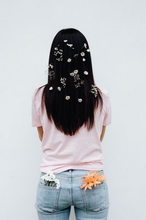 Back view of woman with flowers on her hair and back pockets standing against blue background