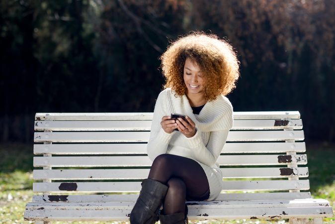 Laughing woman checking her phone and sitting the sun