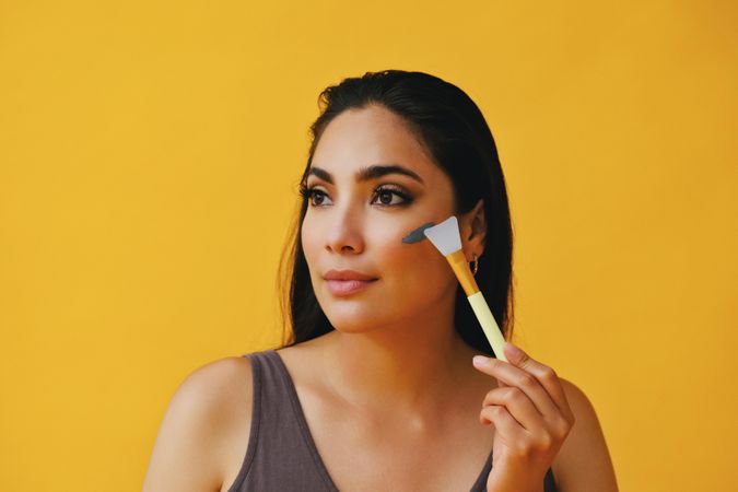 Beautiful Latina woman applying clay mask with brush