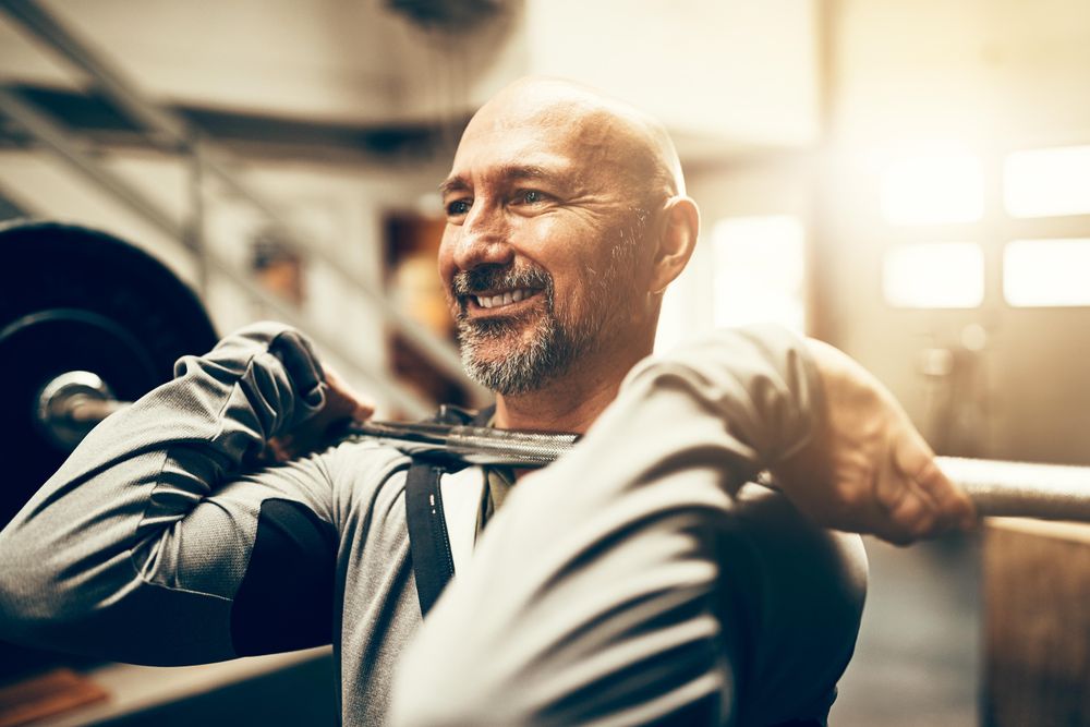 Smiling man holding heavy barbell on shoulders