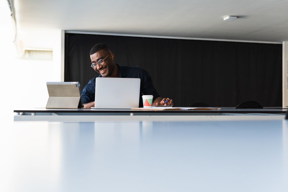 Black guy video chatting on tablet near laptop in workplace