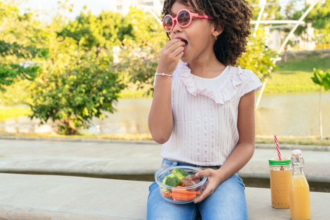 Girl eating vegetables and fruit outdoors at a park
