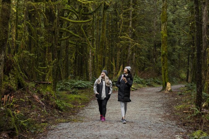 Happy woman and young female hiking among tall trees