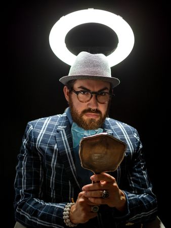 Fashion man in hat holding hand mirror and looking at camera