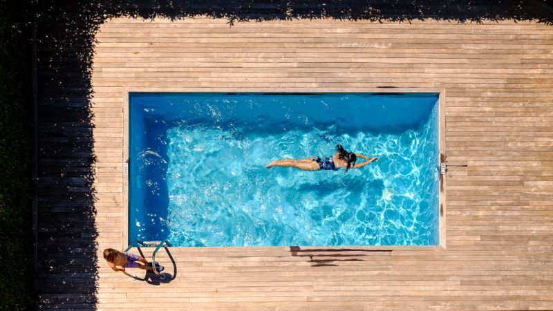 Woman swimming in outdoor pool near son standing on wooden deck