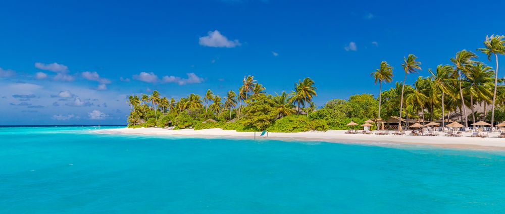 Wide shot of clear blue water and reclining chairs on the beach, wide