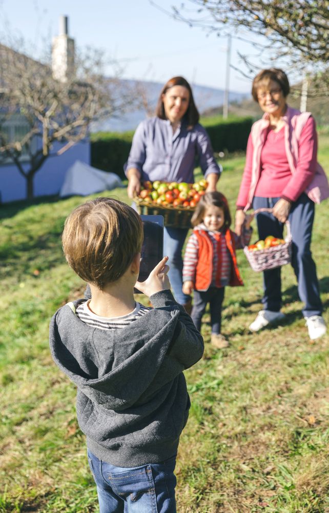 Boy taking photo of family with harvested apples in basket