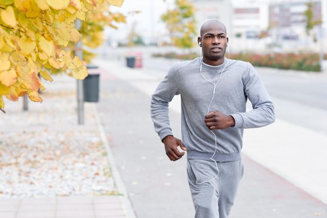 Male jogging in city during fall with autumn trees in background