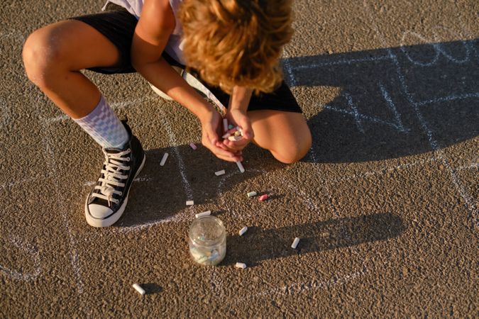 Boy with handful of chalks on asphalt road