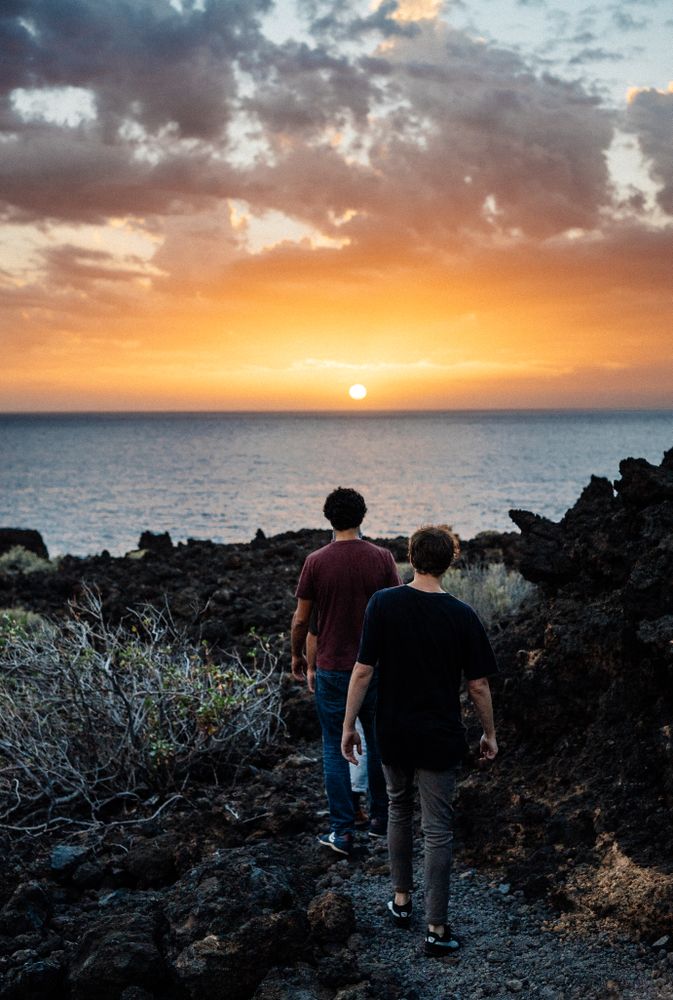 Back of two men walking towards the coast at sunset