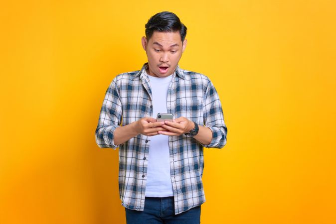 Surprised Asian male looking down at his phone in studio shoot