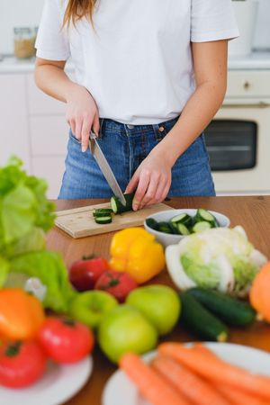 Cropped image of woman slicing a cucumber on brown wooden chopping board