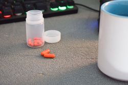 Red pills in container in front of keyboard on desk
