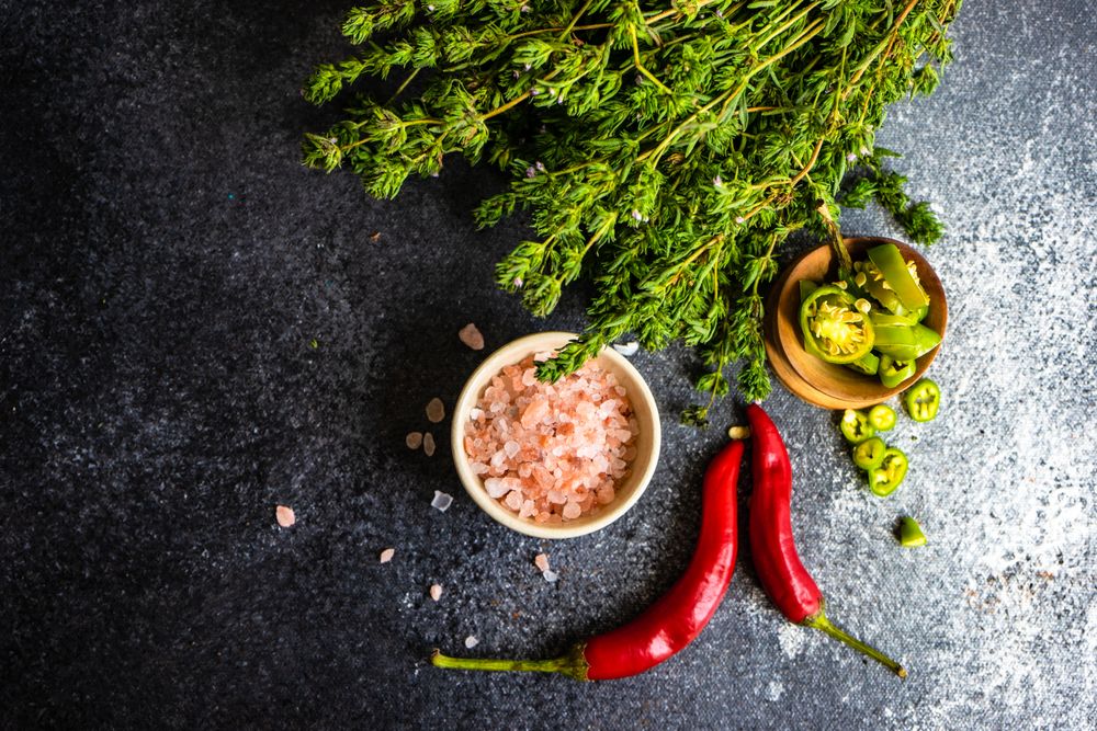Top view of salt, herbs and chili on dark counter