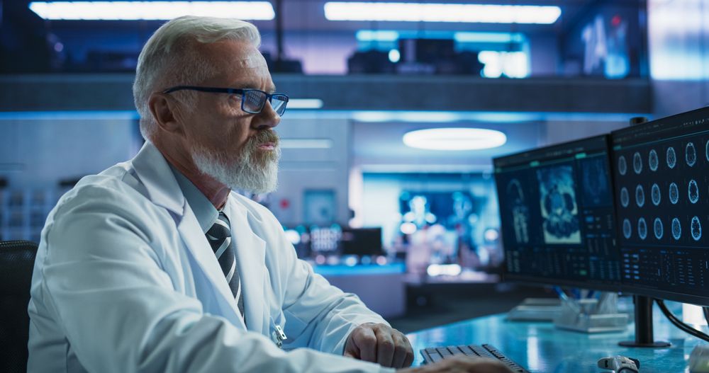 Male Neuroscientist Using Desktop Computer To Analyze MRI Scans Of Brain In Medical Research Center Laboratory.