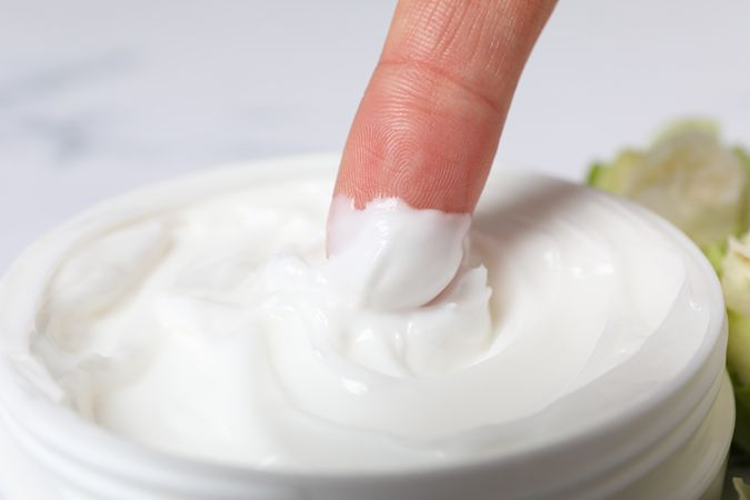 Jar with cream and finger on marble background, close up