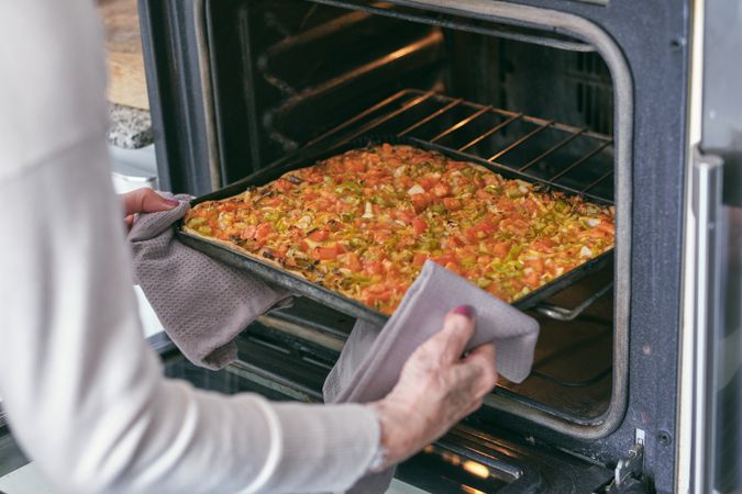 Crop woman putting homemade pizza in oven