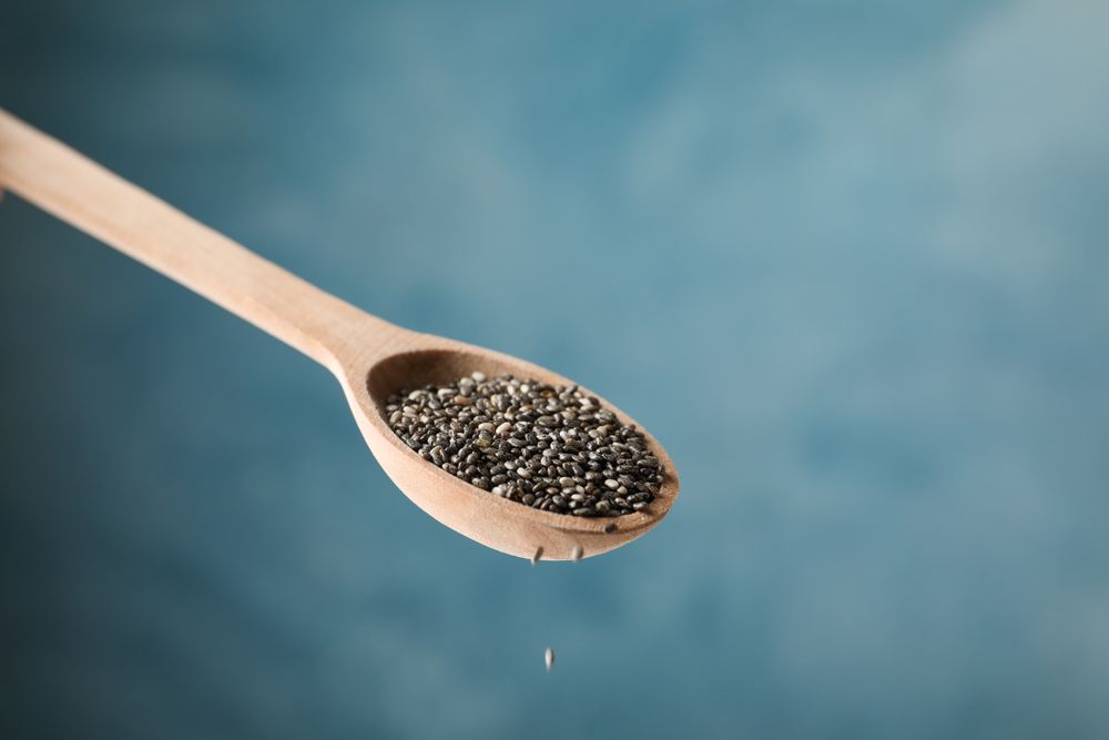 Chia seeds and spoon against blue background, close up