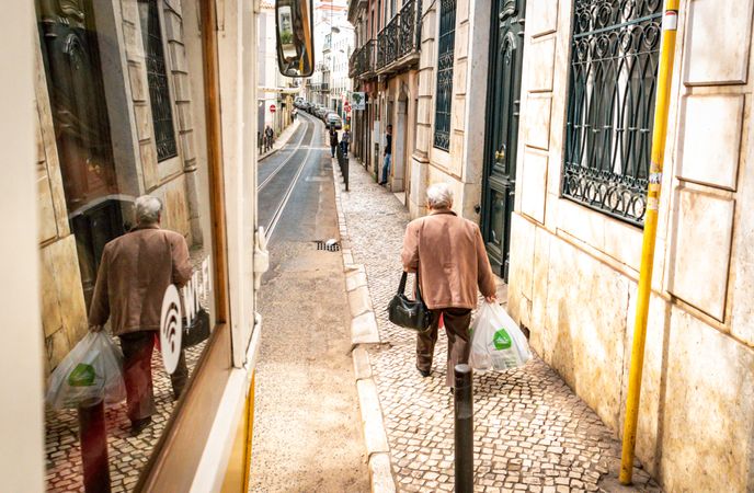 Back view of an older man holding a plastic bag and walking in residential alley