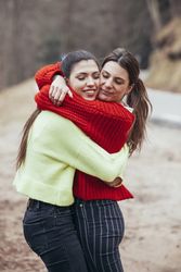 Smiling women in sweaters hugging in park