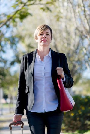 Confident businesswoman walking outside with suit case in hand