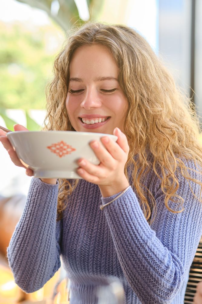 Positive young female and eating soup in restaurant