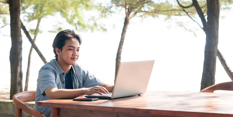 Happy Asian Young businessman work at outdoor with laptop. Concept of remote and freelance work. Young successful man wearing casual blue cloth.