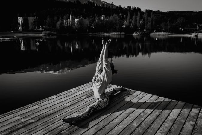 Grayscale photo of woman splitting on wooden dock beside lake in the Austrian Alps
