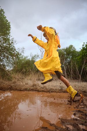 Preteen boy jumping over puddle
