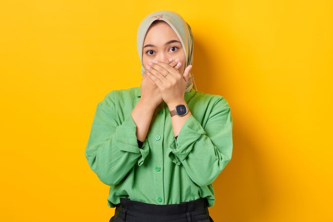 Shocked Muslim woman in headscarf and green blouse with both hands over her mouth