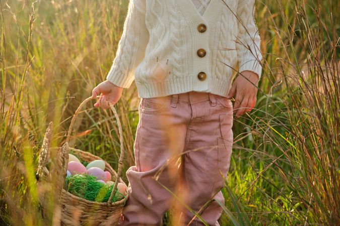 Crop faceless girl carrying basket with Easter eggs in nature