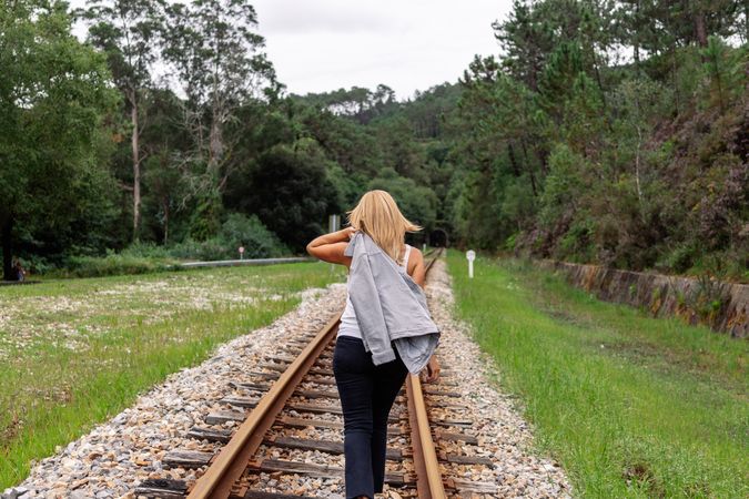 Woman walking along railway though greenery part of road
