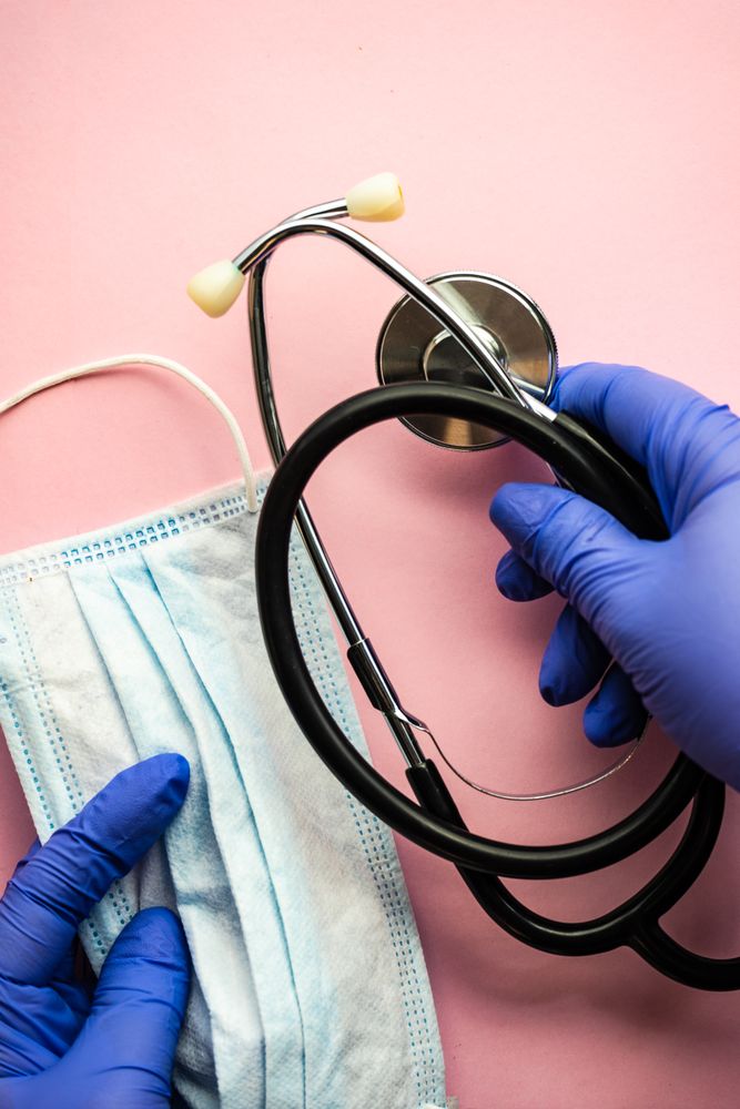 Looking down at pink table with hands holding facemask & stethoscope