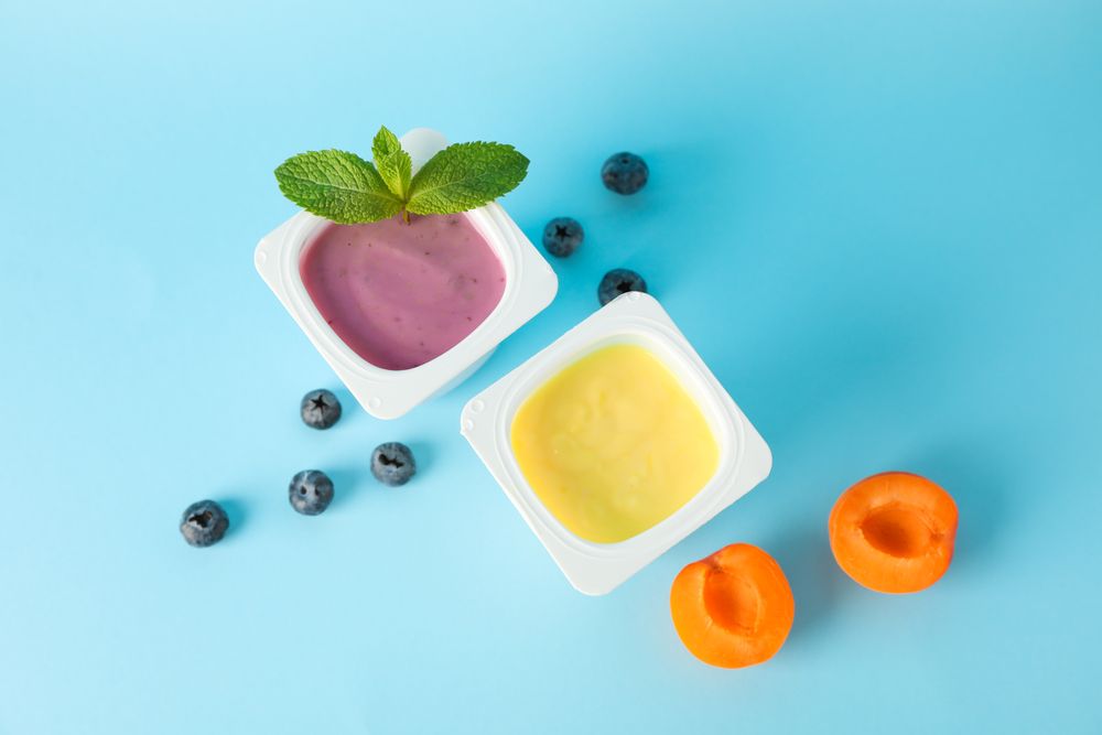 Plastic cups with yogurt and fruits on color background, space for text